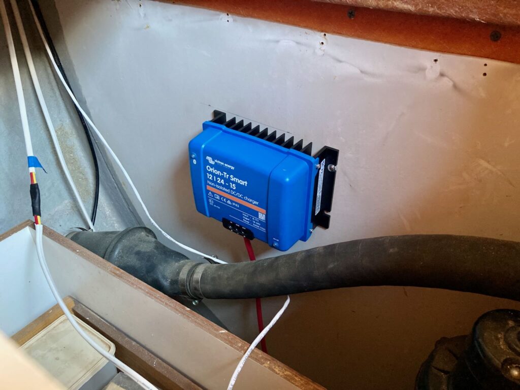 Victron Orion-Tr Smart DC-DC charger mounted on a vertical surface above the exhaust hose and a shelving unit. Several wires are visible in the frame. The charger is not yet fully connected to the wires.